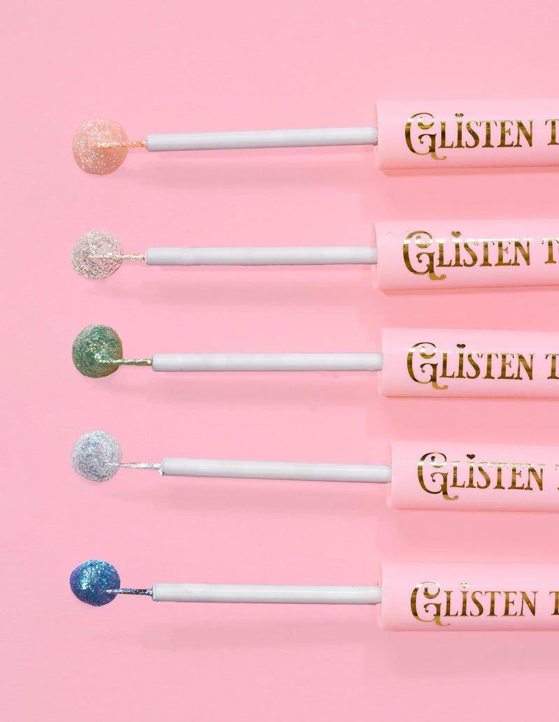 5 delineadores de ojos con purpurina P.Louise Glisten To Your Heart alineados con una gota del producto en el extremo sobre un fondo rosa