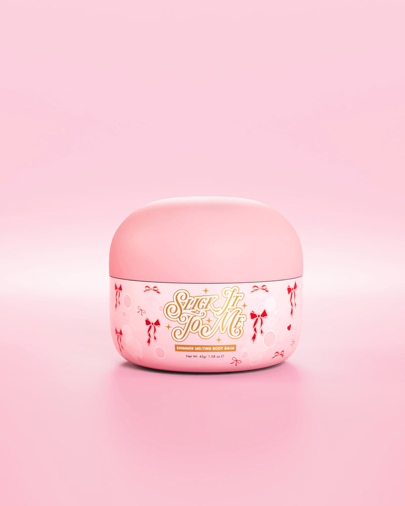 Rosa badekar med SLick It To Me skimmersmeltende kroppsbalsam med dekorative røde sløyfeelementer på en rosa bakgrunn