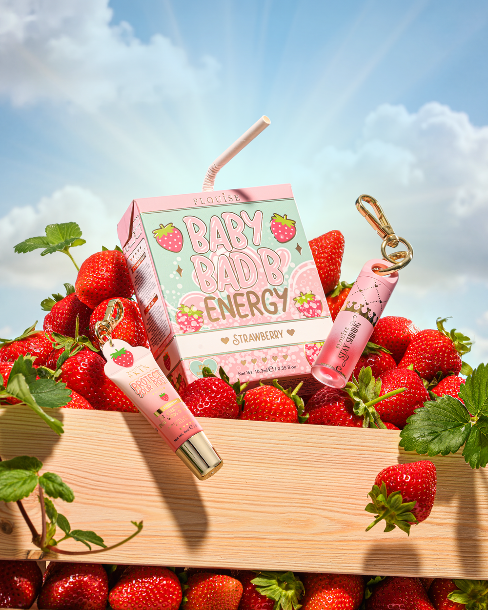 P.Louise Strawberry Baby Bad B Mini Lip Oil και Mini Lip Conditioner σε ένα τραπέζι που περιβάλλεται από φράουλες