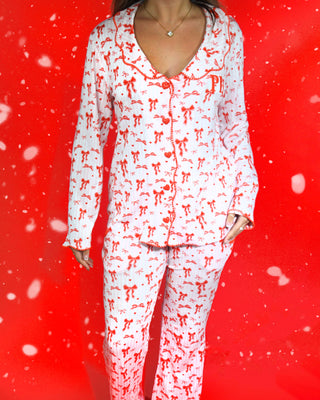 Bild av en kvinnas kropp som bär en festlig uppsättning rosa och vitrandiga pyjamas med röda rosettdesigner på dem mot en röd bakgrund och snöflingor