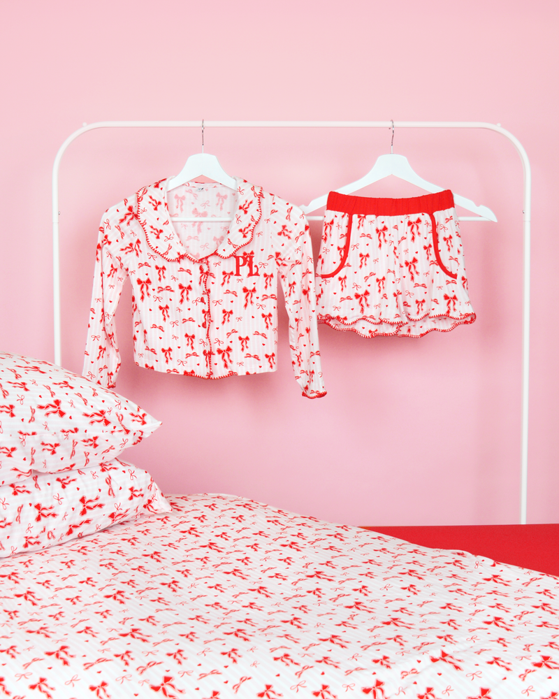 Conjunto de niñas de rayas rosas y blancas P.Louise pantalones cortos de pijama con lazo navideño en perchas en un dormitorio rosa con ropa de cama a juego 