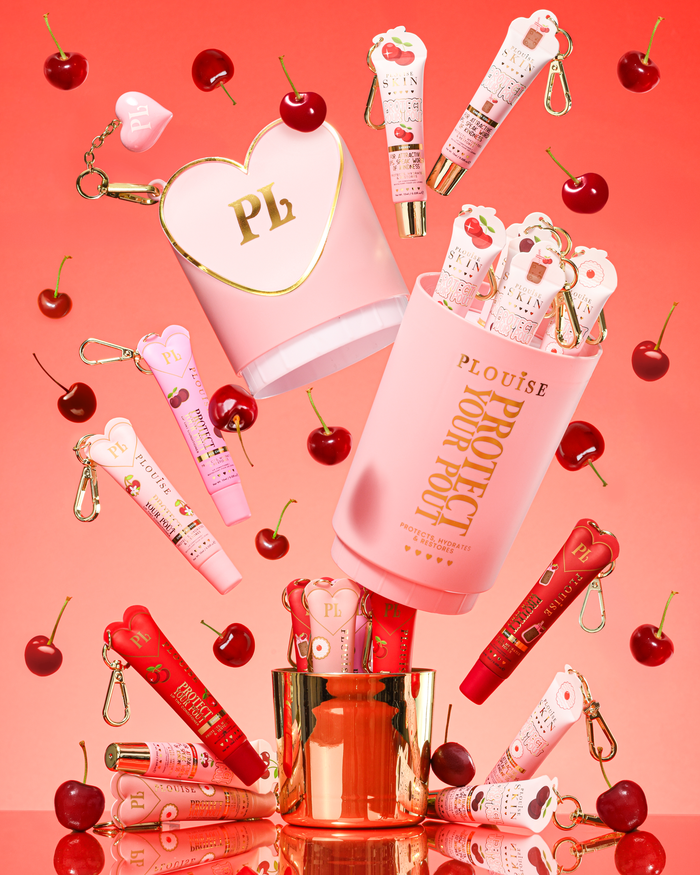 Pink XL Protect Your Pout Geschenkset, das geöffnet ist, umgeben von Kirschen und rosa und roten Lippenpflegemitteln auf einem rosa Hintergrund