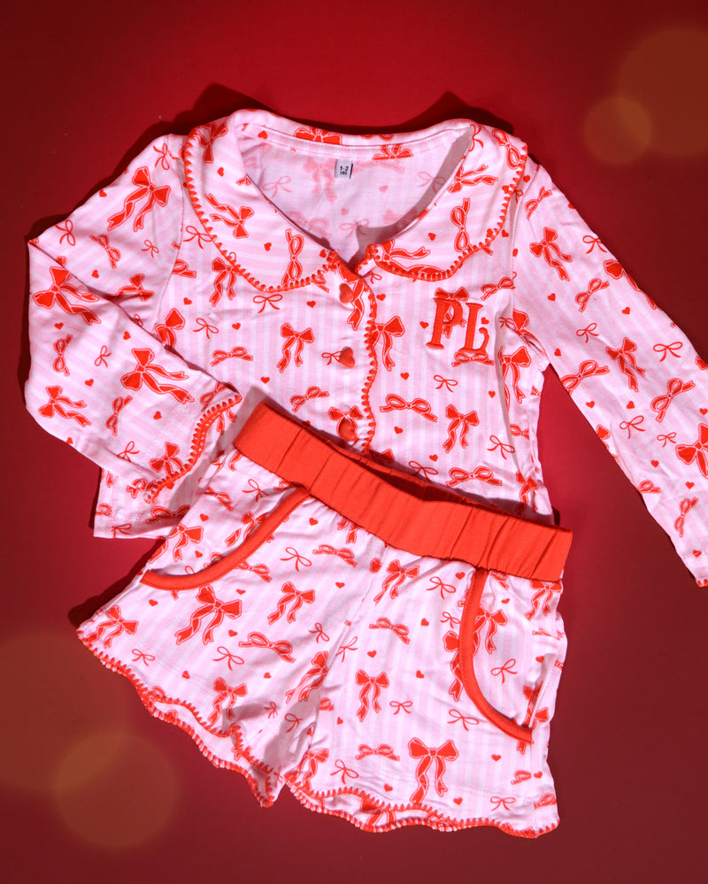 Conjunto de pijamas navideños para niños de rayas rosas y blancas con diseños de lazos rojos sobre un fondo rojo