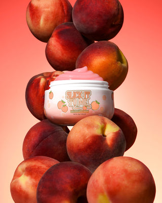 Frasco de P. Louise Slick It To Me Peach Melting Body Balm com creme rosa cercado por pêssegos em um fundo gradiente