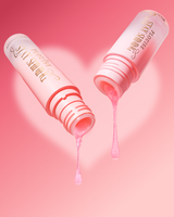 Two pink cosmetic tubes labeled 'STAY SHINING' shown on a pink background with a heart shape behind them. Pink gel is dripping from both open tubes, with one drop falling below and another above.