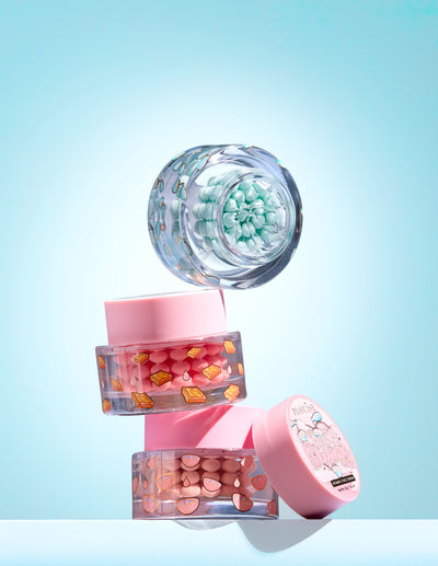 Tre vasetti con capsule colorate di vitamina C in gel su sfondo azzurro
