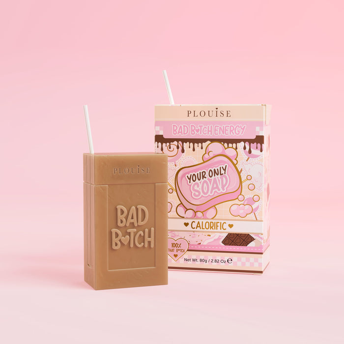 Et brunt stykke sæbe med 'Bad Bitch' indgraveret, ledsaget af en farverig juicebokspakke med 'Calorific' mærket på, præsenteret på en lyserød baggrund.