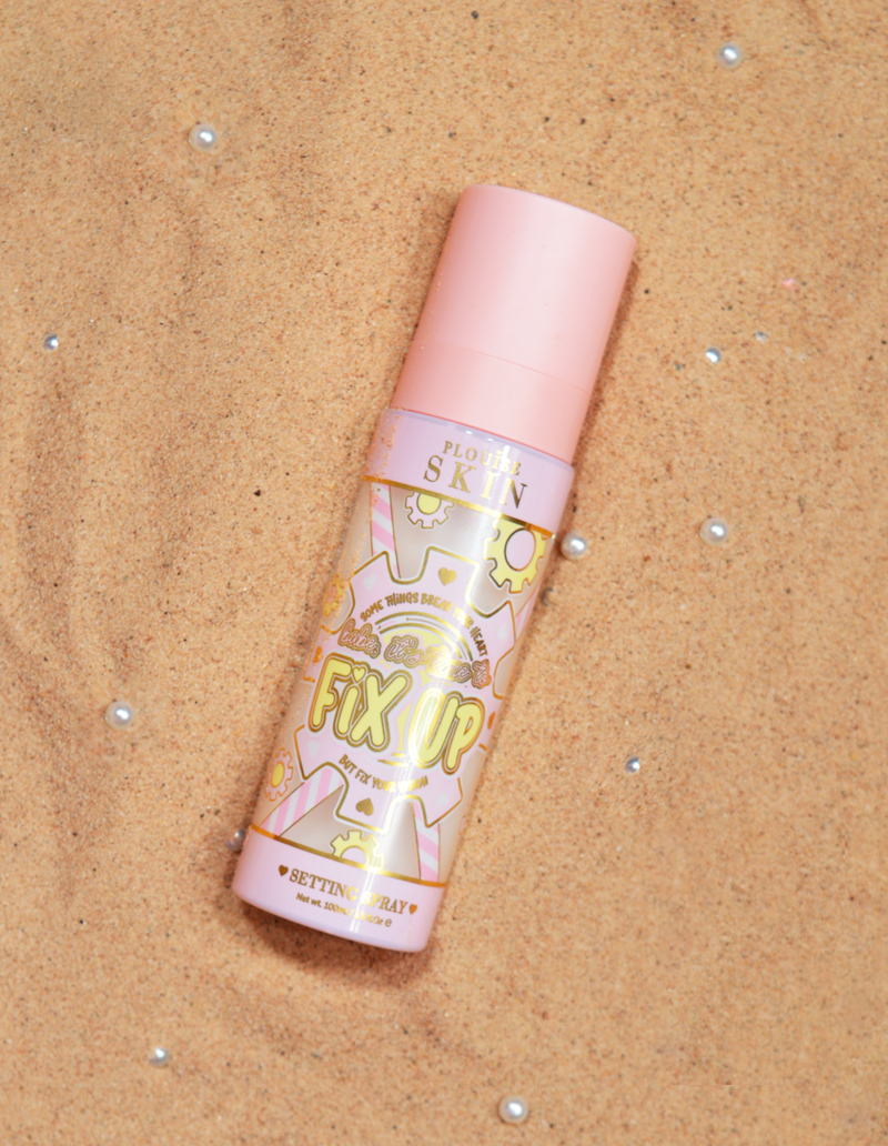 Bočica P.Louise Fix Up Mattifying Setting Spray s ružičastim čepom i ukrasnim uzorcima na etiketi, izložena na pješčanoj površini.