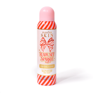 Een fles P. Louise Ready Set Sparkle Christmas Glitter Setting Spray met rode en roze strepen op de fles en een rood en roze gestreepte strik tegen een witte achtergrond