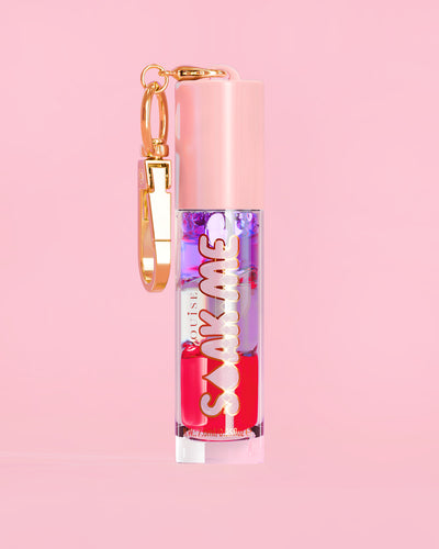 P. Louise Soak Me Lip Oil med farverig lagdelt olie i et lyserødt rør med en guldlås på en lyserød baggrund